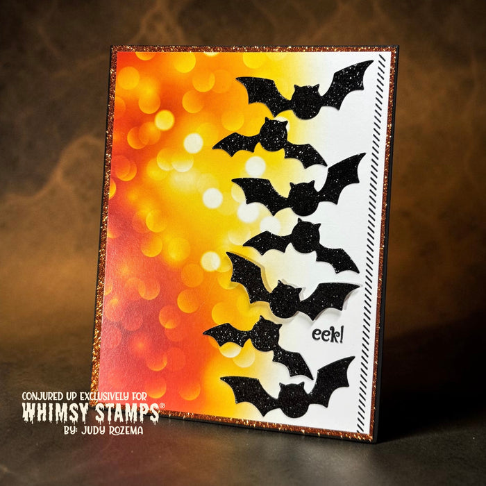 A handmade Halloween card featuring black glitter bat die-cuts layered over a white and orange gradient background with bokeh sparkle effects.