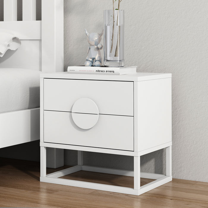 Abigail 55cm 2-Drawer Bedside Table w/ Handle - White beside a bed, featuring arc handles, atop a metal base, with a book, geometric bear figurine, and vase on its surface.