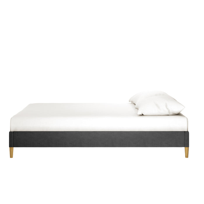 Celina Boucle Upholstered Fabric Bed Base - Black Queen features a dark-gray upholstered platform design with short wooden legs, topped with a white mattress and pillow against a plain white background.