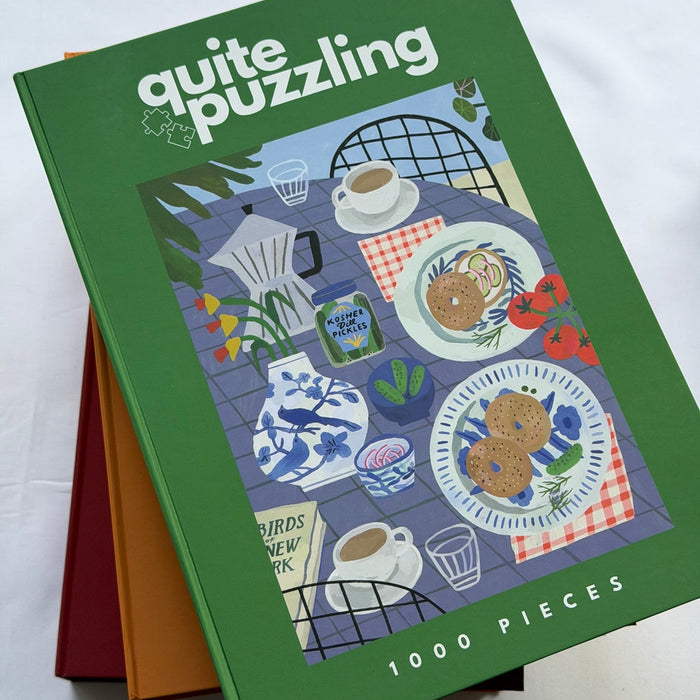The "Half-Sour Sundays" 1,000 piece puzzle by Quite Puzzling features a New York breakfast scene on a blue checkered table—an ideal coffee table challenge for puzzle lovers.
