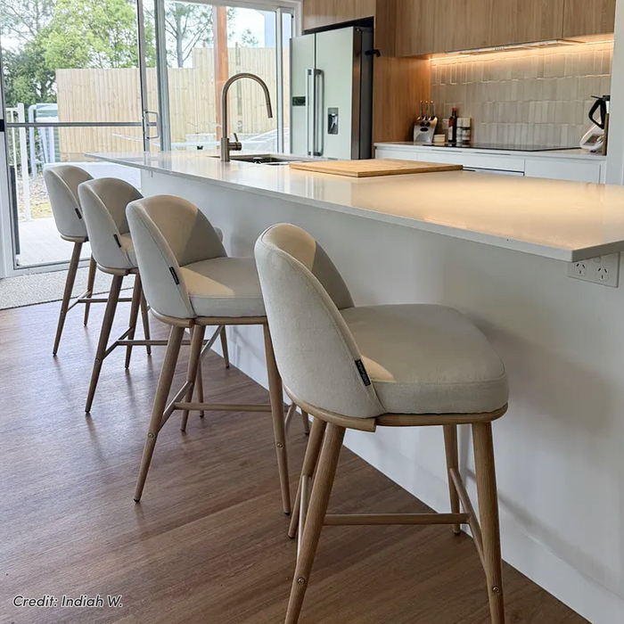 Jeremi high back linen bar stool in wheat with oak legs, shown at a white kitchen island