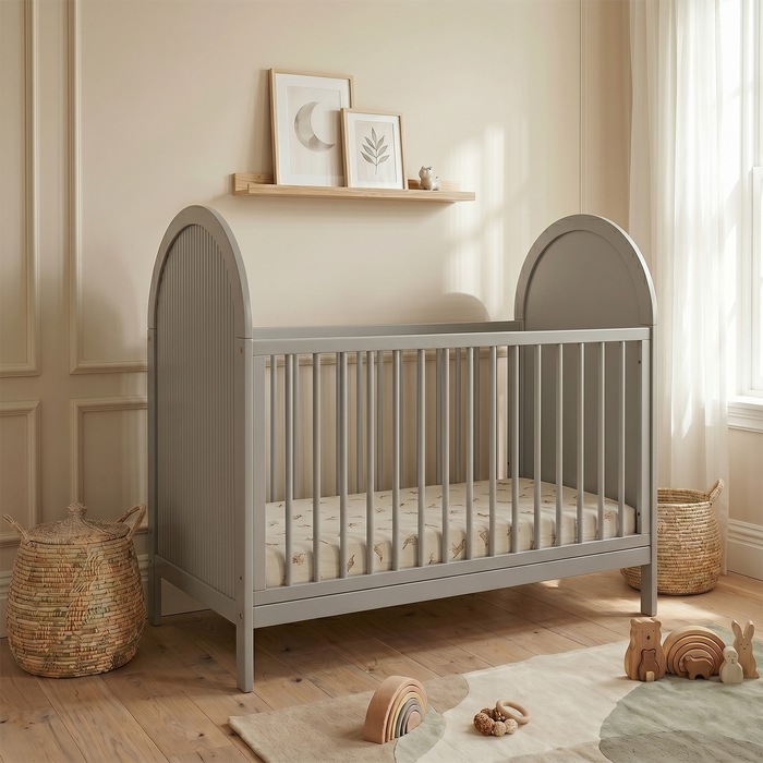 Grey crib in a styled nursery room with decorative baskets and toys