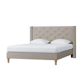 Maggie Queen Winged Fabric Bed Frame in Warm Grey features a tall, button-tufted headboard, low-profile frame, turned wooden legs, white mattress cover, and pillows, embodying elegance and stability.