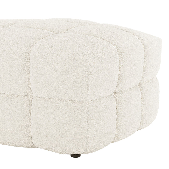 The Norah Boucle Ottoman in Cream White features a low, round design with quilted square panels in bouclé fabric, showcasing a small, dark foot at the base.