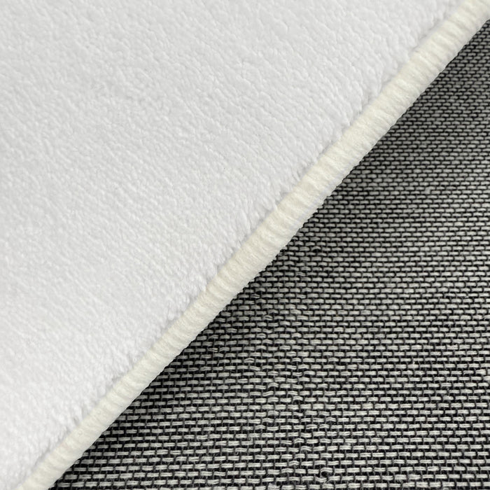 Close-up of Pixie 240x330cm Large Wavy Shag Rug in Cream White, showcasing its soft, fleece-like texture with a bound edge atop a woven grey-tone fabric background.