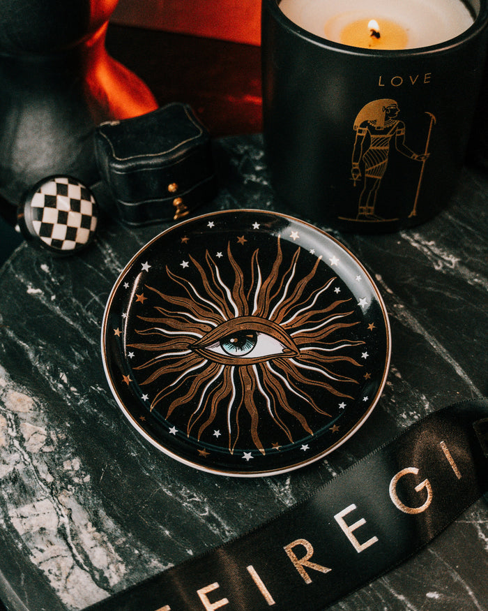 Decorative plate with eye design on a dark surface with a candle and ribbon.