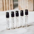 Five small perfume bottles with black caps on a marble surface