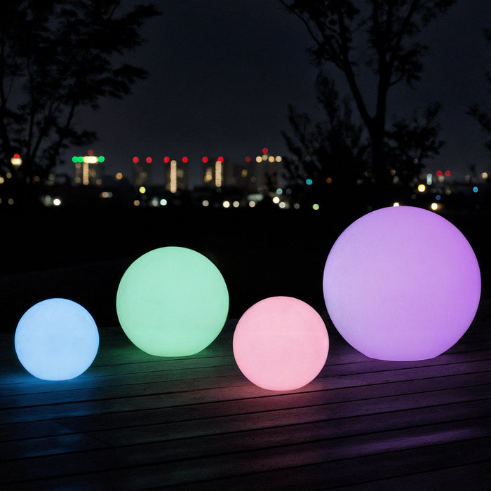 Sphero 40cm Floating Waterproof Outdoor LED Ball Lights glowing in blue, green, pink, and purple on a wooden patio at night, enhancing the ambiance with a city skyline backdrop.