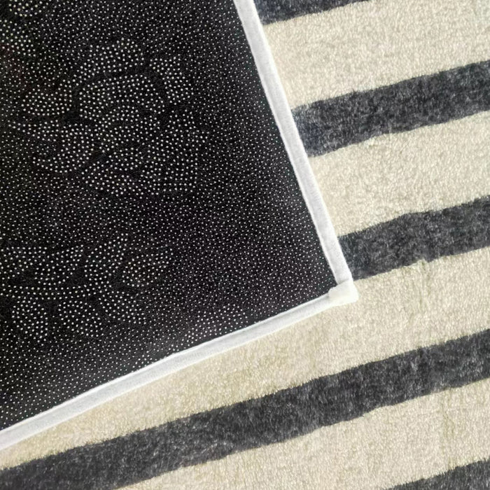 Vannebo Modern Abstract Floor Rug 200 x 300cm with a black surface featuring white, grippy dots forming floral patterns, layered over a cream-and-dark-gray striped rug, showcasing modern design and texture.